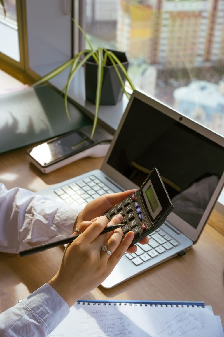 شخص يستخدم آلة حاسبة وحاسوبًا محمولًا مع مستندات العمل